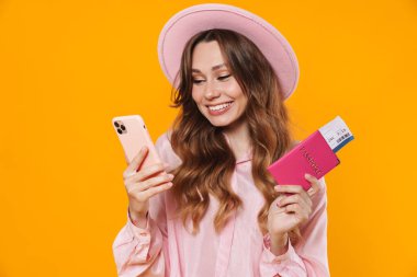 Sarı arka planda bilet ve cep telefonlu, şapkalı gülümseyen bir kadın resmi