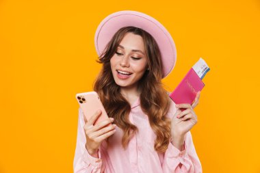 Sarı arka planda bilet ve cep telefonlu, şapkalı gülümseyen bir kadın resmi
