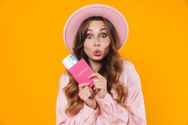 Şapkalı, elinde pasaportu olan ve sarı arka planda öpüşen bir kadın resmi.