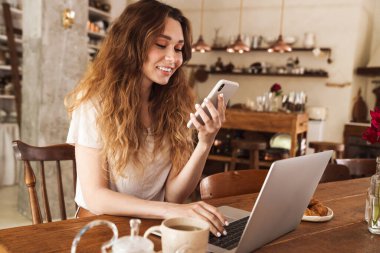 Mutfak masasında oturan, cep telefonu kullanan güzel, genç bir kız.