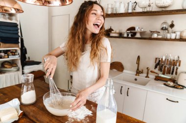 Çekici, genç, neşeli kız mutfakta yemek pişiriyor, para kazanıyor.