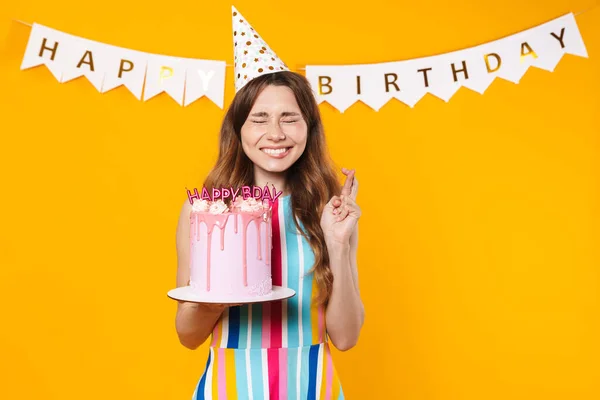 幸せな女性のイメージでパーティーコーン保持Torteと指交差しましたのために幸運絶縁上の黄色の背景 — ストック写真