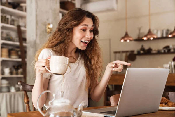 아름다운 소녀가 식탁에 노트북 컴퓨터를 사용하고 비디오 커피마시기 — 스톡 사진