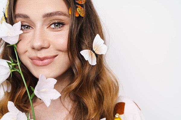 Фото веселой женщины с фальшивыми бабочками и цветком, улыбающимся в камеру, изолированную над белой стеной
