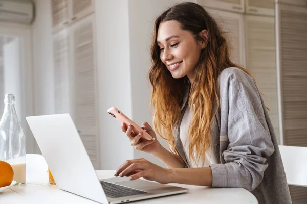 Hübsche Fröhliche Junge Frau Frühstückt Während Sie Küchentisch Sitzt Laptop — Stockfoto