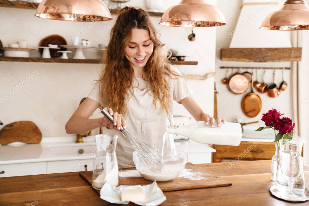 Attractive young cheerful girl baking at the kitchen, making dough