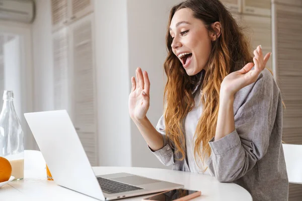 Kızıl saçlı kadının portresi. Parlak mutfakta dizüstü bilgisayarla çalışırken şaşkınlığını dile getiriyor.