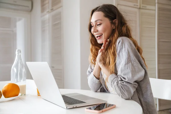 Portrait of ginger excited woman expressing surprise while working with laptop in bright kitchen