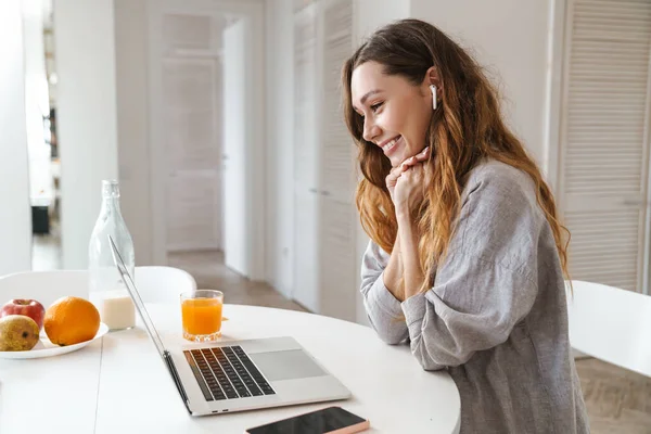 Mutfak masasında oturmuş video görüşmesi yaparken oldukça neşeli genç bir kadın kahvaltı yapıyor.