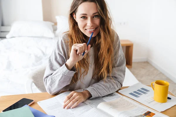 Yatak odasında ödev yaparken egzersiz kitabına yazan gülümseyen güzel öğrenci kadının fotoğrafı.