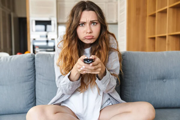 Jovem Perturbada Relaxando Sofá Casa Segurando Controle Remoto — Fotografia de Stock