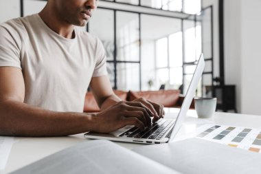 Oturma odasında otururken dizüstü bilgisayarla çalışan odaklanmış Afro-Amerikan bir adamın kesilmiş fotoğrafı.