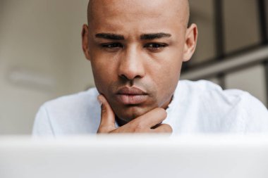 Bilgisayarla çalışan ve oturma odasında düşünen ciddi bir Afrikalı Amerikalının fotoğrafı.