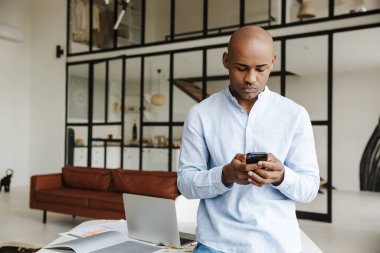 Afro-Amerikan bir adamın oturma odasında çalışırken cep telefonu kullanması.