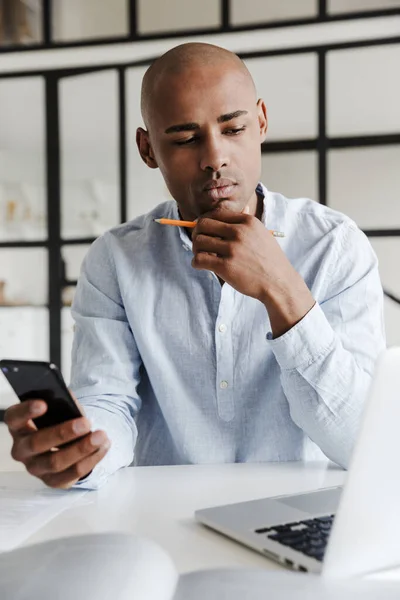 Foto Homem Afro Americano Sério Usando Telefone Celular Enquanto Trabalhava — Fotografia de Stock