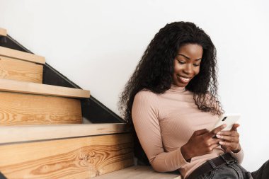 Evdeki merdivenlerde cep telefonu kullanan güzel, sevimli, Afrikalı bir kadının görüntüsü.