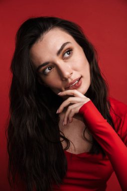 Esmer, çekici bir kadının kırmızı arka planda yalnız poz verirken ve yan yana bakarken fotoğrafı.