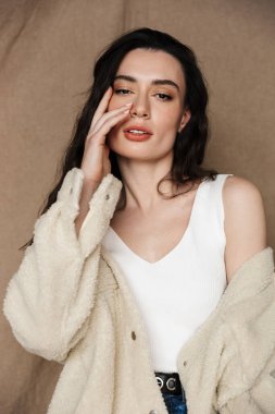 Ceketli baştan çıkarıcı genç bir kadının bej arka planda izole edilmiş poz veren ve kameraya baktığı fotoğraf.