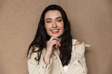 Ceketli neşeli genç bir kadının bej arka planda izole edilmiş kameraya bakıp güldüğü fotoğraf.