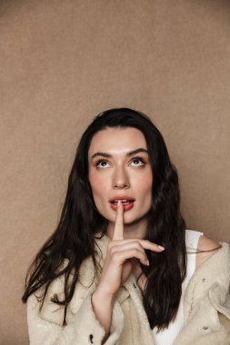 Beyaz ceketli güzel bir kadının bej arka planda izole edilmiş kamerada sessiz bir jest göstermesi.