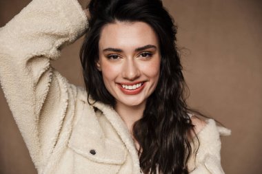 Bej arka planda izole edilmiş, gülen ve kameraya bakan komik, sevimli bir kadının yakın çekimi.