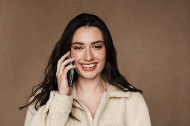 Ceketli, gülümseyen ve cep telefonuyla konuşan güzel bir kadının fotoğrafı.