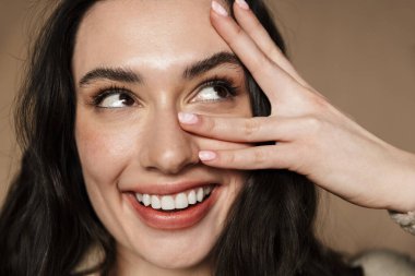 Mutlu, esmer, tatlı bir kadının bej arka planda sırra kadem basmış gülüşünün yakın bir fotoğrafı.