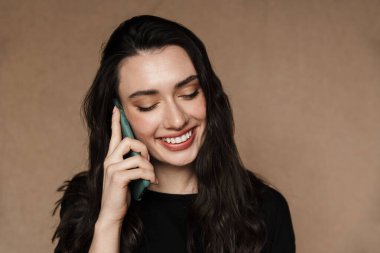 Bej arka planda izole edilmiş, gülümseyen ve konuşan güzel esmer kadının fotoğrafı.