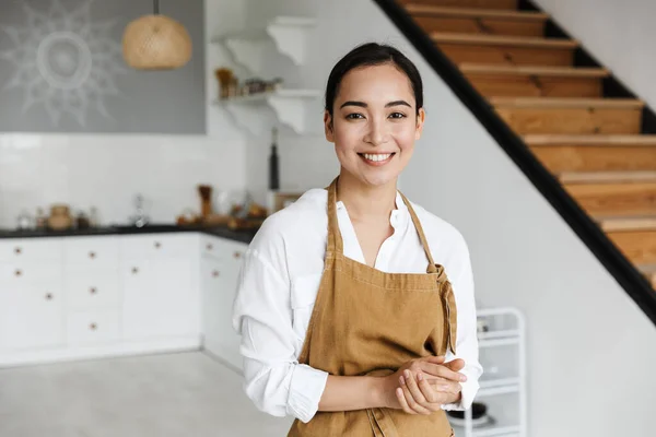 笑顔魅力的な若いですアジアの女性身に着けていますエプロン立ってキッチンに自宅 — ストック写真