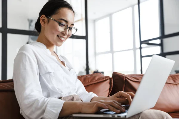 魅力的な笑顔若いアジアのビジネス女性は 自宅で革のソファでリラックスし ラップトップコンピュータで作業 — ストック写真