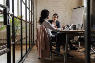 Modern bir ofiste yeni bir proje üzerinde çalışan iki çekici, zeki, çok ırklı kadın girişimci masa başında oturuyorlar.