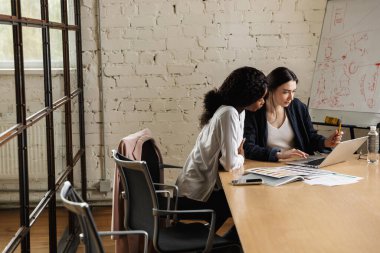Modern bir ofiste yeni bir proje üzerinde çalışan iki çekici, zeki, çok ırklı kadın girişimci masa başında oturuyorlar.
