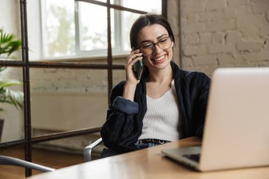 Ofis masasında oturup cep telefonuyla konuşurken dizüstü bilgisayarda çalışan kendine güvenen genç girişimci.