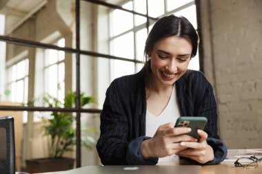 Ofis masasında oturan, cep telefonu kullanan, kendine güvenen, çekici, genç bir girişimci.