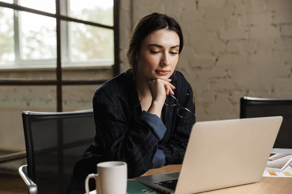 自信而又有魅力的年轻女企业家坐在写字台前 在笔记本电脑上工作 — 图库照片