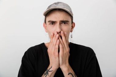 Siyah elbiseli korkmuş bir gencin portresi kameraya bakıyor ve beyaz arka planda ağzını kapatıyor.