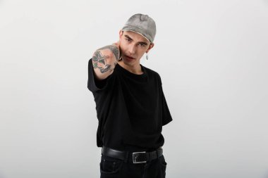 Siyah giyinmiş, beyaz arka planda poz veren cesur, kendine güvenen bir adamın portresi.