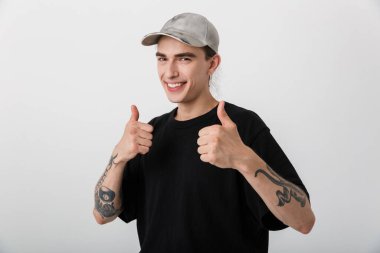 Siyah elbiseli mutlu bir gencin portresi başparmağını kaldırıyor ve beyaz arka planda gülümsüyor.