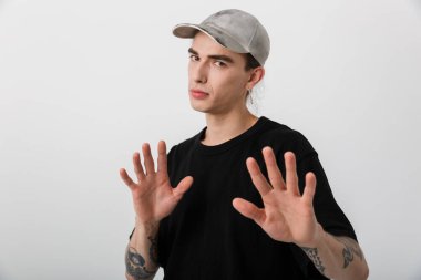 Siyah elbiseli beyaz bir adamın portresi. Kameraya bakıyor ve beyaz arka planda dur işareti yapıyor.