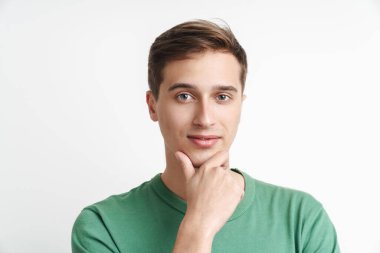 Basit tişörtlü beyaz bir adamın beyaz arka planda izole edilmiş bir şekilde kameraya bakıp çenesine dokunuşu.