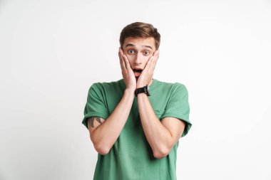 Şok olmuş, beyaz tişörtlü, stresli beyaz bir adamın beyaz arka planda izole edilmiş yüzünü tutuşu.