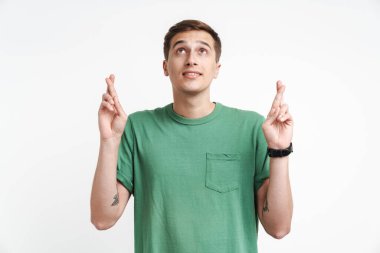 Beyaz arka planda dua eden ve parmaklarını çapraz yapan beyaz tişörtlü beyaz bir adam resmi