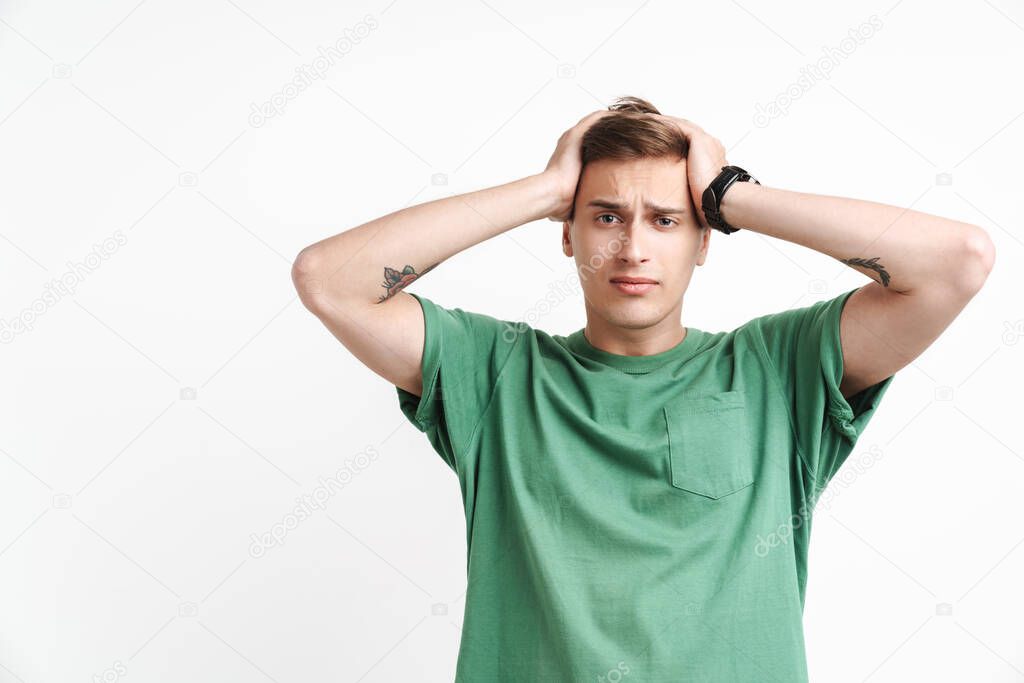 Image of handsome caucasian man in basic t-shirt being stressed and grabbing his head isolated over white background