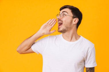 Gözlüklü beyaz bir gencin fotoğrafı. Sarı arka planda izole edilmiş bir şekilde poz verip çığlık atıyor.