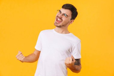 Gözlüklü heyecanlı genç adamın sarı arka planda izole edilmiş bir jest yaptığı fotoğraf.