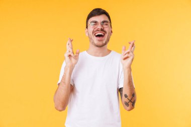 Gözlüklü heyecanlı genç adamın fotoğrafı sarı arka planda iyi şans jesti yapıyor.