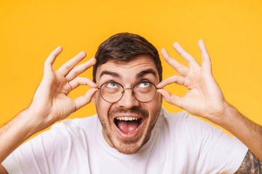 Gözlüklü heyecanlı genç adamın yakından çekilmiş fotoğrafı şaşırdığını ve sarı arka planda izole bir şekilde yukarıya baktığını gösteriyor.