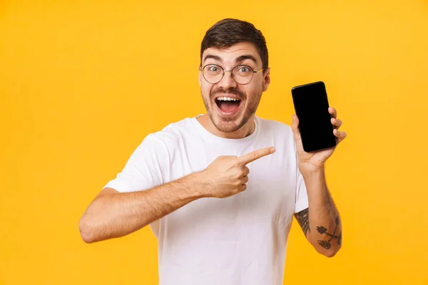 照片上 快乐的年轻人戴着眼镜 手拿着手指对着黄色背景下的手机 — 图库照片