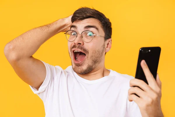 Zdjęcie Przystojnego Mężczyzny Okularach Trzymającego Smartfona Wyrażającego Zaskoczenie Żółtym Tle — Zdjęcie stockowe