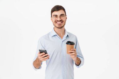 Gözlüklü, kahve içen ve beyaz arka planda izole edilmiş cep telefonu kullanan mutlu beyaz adamın fotoğrafı.